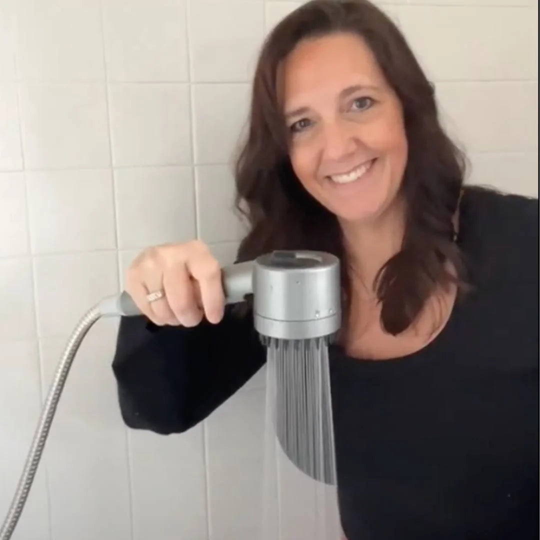 Smiling woman demonstrating the FlowMist high-pressure filtered showerhead in her bathroom, showing powerful water flow during use.